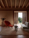Red Oda Lounge Chair and Radiohus Sofa in a rustic room with an Androgyne Table, Plinth Pedestal, and open doorway.