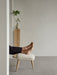 A person rests their bare feet on the Oda Ottoman with its light fabric upholstery and natural oak legs in a minimal setting.