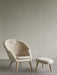 A cream-coloured Oda Lounge Chair with a curved back and oak legs, sits next to the matching Oda Ottoman on a grey floor.