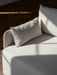 A shot of a light grey upholstered sofa with a plush cushion. Sunlight creates strong shadows across the textured fabric.