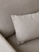 A close-up shot of a beige, textured fabric corner of a sofa or armchair, with a matching cushion resting against the back.