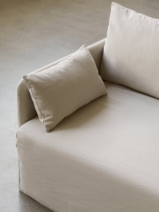 A close-up, high-angle shot of a sofa upholstered in a light beige, textured fabric, with soft cushions, on a concrete floor.