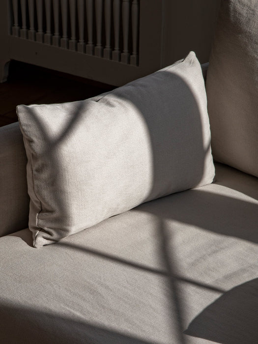 Detailed shot of the Offset Sofa's cushion, showing its light, textured loose cover with sunlight and shadow play across it.