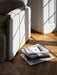 Sunlight casts a window shadow on the arm of the Offset Sofa w. Loose Cover. A pile of books sits on the herringbone floor.