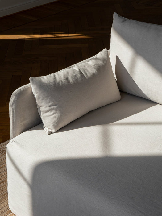 Sunlight falls on the textured, light-coloured fabric of the Offset Sofa w. Loose Cover, highlighting a cushion and arm.