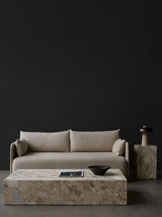 Beige Offset Sofa before a dark wall, styled with a Plinth Grand table, Plinth Tall table, and a Reverse Table Lamp.