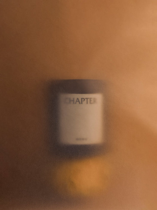 An Olfacte Scented Candle, Chapter, seen through a textured, amber-toned frosted glass, creating a soft and atmospheric mood.