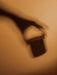 An artistic, blurry shadow of a hand holding the Olfacte Scented Candle, Chapter, against a warm, textured background.
