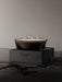 The four-wick Olfacte Scented Candle, Midnight Soak, glows in a dark glass bowl atop its black packaging. A twig rests below.