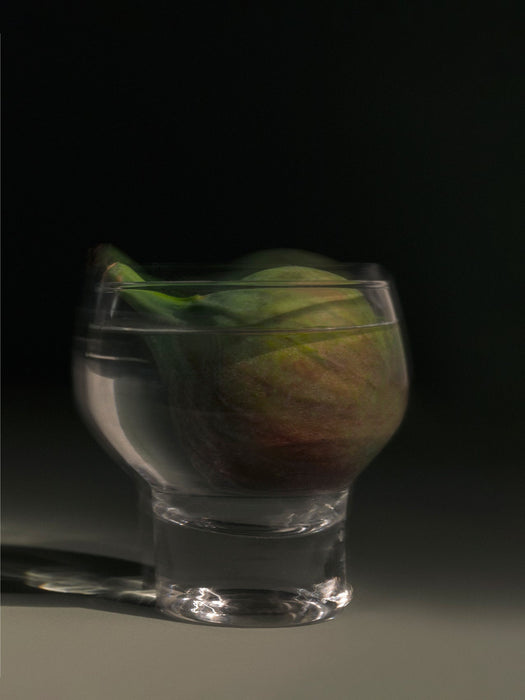A moody, artistic photo of a fig submerged in a glass of water against a dark background for the Midnight Soak candle.
