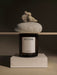 The Olfacte Scented Candle, Wet Ink, in its dark jar, is styled on a plinth below a shelf with a stone and dried moss.