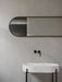 The black-framed Norm Oval Mirror mounted horizontally on a grey bathroom wall, above a white oval sink with a black tap.