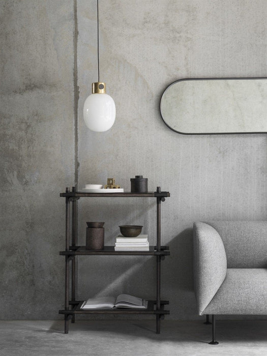 The black-framed Norm Oval Mirror hangs horizontally on a concrete wall above a dark wood shelf and next to a grey sofa.