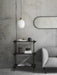 The black-framed Norm Oval Mirror hangs horizontally on a concrete wall above a dark wood shelf and next to a grey sofa.
