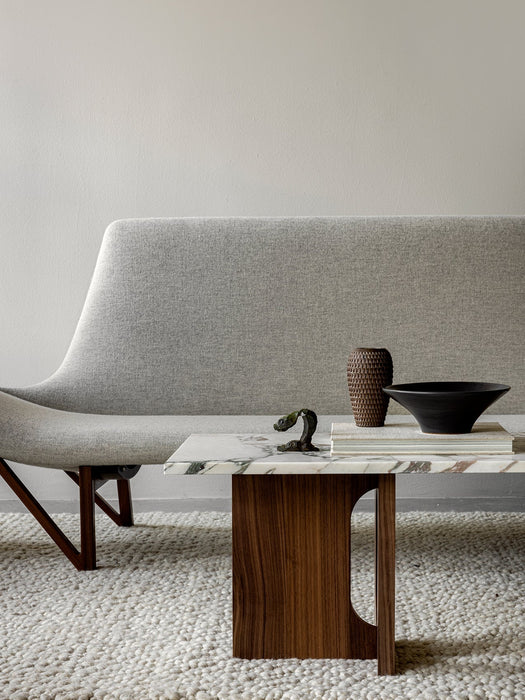 Side view of the grey Pagode Sofa next to an Androgyne Lounge Table with a marble top and wood base on a thick white rug.