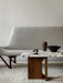 Side view of the grey Pagode Sofa next to an Androgyne Lounge Table with a marble top and wood base on a thick white rug.