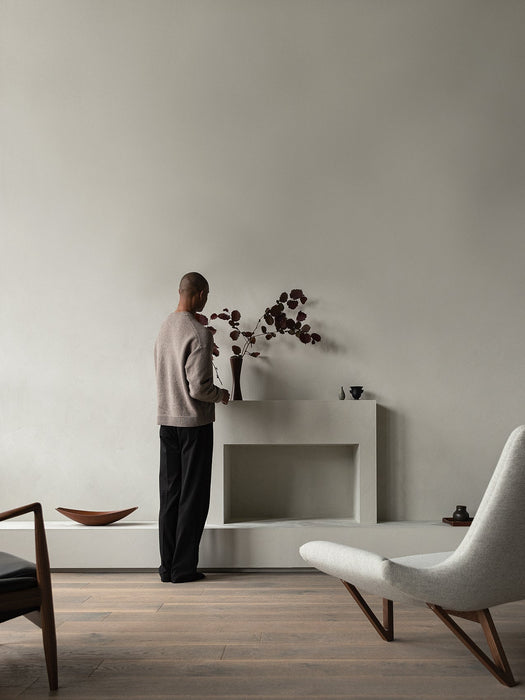 A person stands by a modern fireplace in a minimalist living room. In the foreground is the Pagode Sofa in light grey fabric.