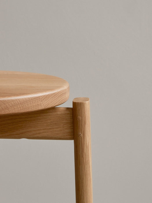 Detailed close-up of the Passage Bar Stool in natural solid oak, showing the wood grain on the round seat and its joinery.