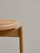 Detailed close-up of the Passage Bar Stool in natural solid oak, showing the wood grain on the round seat and its joinery.
