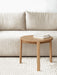 A close-up of a round oak Passage Lounge Table with two white books, set against a beige Offset Sofa and on a Houkime Rug.
