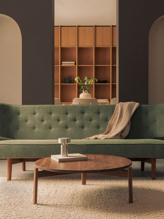 The round walnut Passage Lounge Table with a Column Table Lamp, before a green tufted Radiohus Sofa on a beige rug.