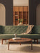 The round walnut Passage Lounge Table with a Column Table Lamp, before a green tufted Radiohus Sofa on a beige rug.