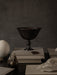 The Audo Pavot Bowl in a dark finish, styled on a stack of books in a moody still life with a bronze pear and an ostrich egg.