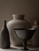 The dark bronze Pavot Bowl on a pedestal in a still life with a slender dark vase and two larger, textured beige vases.