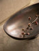 Close-up, angled view of the Pavot Centerpiece, a dark bronze bowl with a flowering branch inside, on a stone surface.