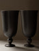 A close-up of two Pavot Vases by Audo, featuring a dark, matte bronzed finish and a classic goblet shape with a flared rim.