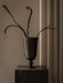 The black, chalice-shaped Pavot Vase holding sculptural, dried branches, on a dark marble plinth against a neutral backdrop.