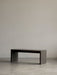 The dark marble Plinth Bridge, a long minimalist table, in a simple room with a concrete floor and grey wall.