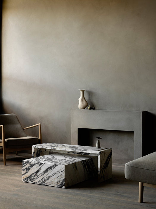 The Seal Lounge Chair next to a marble Plinth Bridge and Plinth Low table set in a modern, grey-toned room by a fireplace.