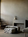The Seal Lounge Chair next to a marble Plinth Bridge and Plinth Low table set in a modern, grey-toned room by a fireplace.