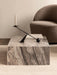 A Plinth Low coffee table in Grey Galaxy Marble, styled with a book and black candelabra, beside a brown Tearoom Lounge Chair