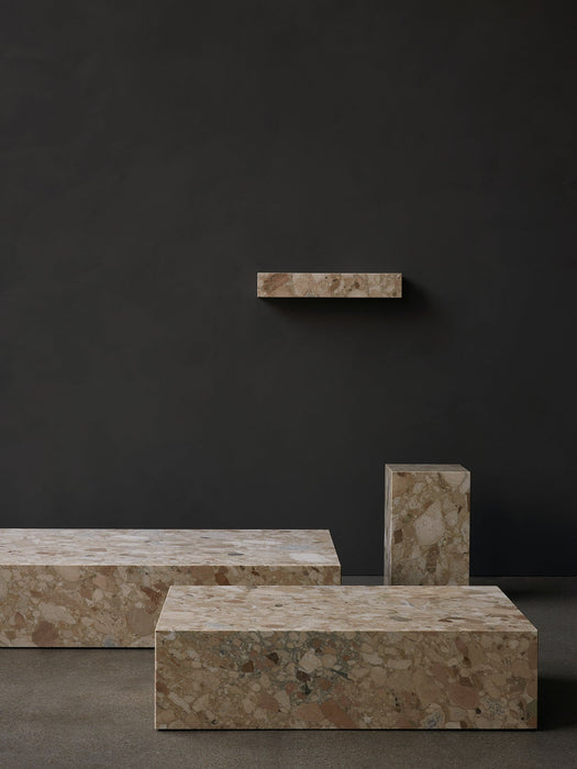 The Plinth collection in Kunis Breccia stone. Two Plinth Low tables, a tall plinth, and a shelf against a dark grey wall.