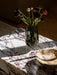 Close-up of the Plinth Low table in Calacatta Viola marble, featuring a dark green vase with red flowers and a wooden bowl.