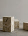 A collection of Plinth Low, Tall, and Grand tables in Kunis Breccia stone, arranged on a concrete floor against a pale wall.