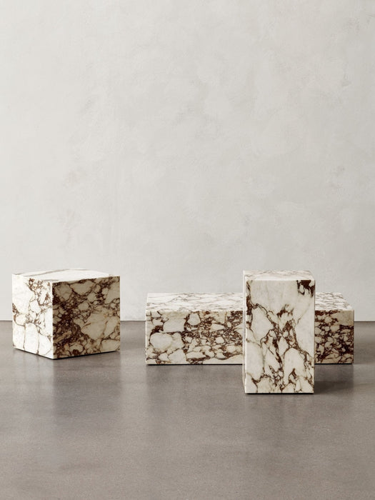An arrangement of four Plinth Low tables in Calacatta Viola marble, showcasing cubic and rectangular forms on a grey floor.