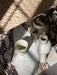 Close-up of the Plinth Low in Calacatta Viola marble, styled with a rustic ceramic teapot, cup, and vase under sunlight.