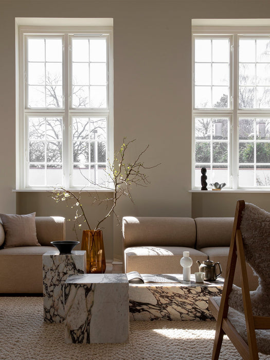 A bright, sunlit living room with two Plinth Low tables in Calacatta Viola marble, styled next to a beige sofa on a rug.
