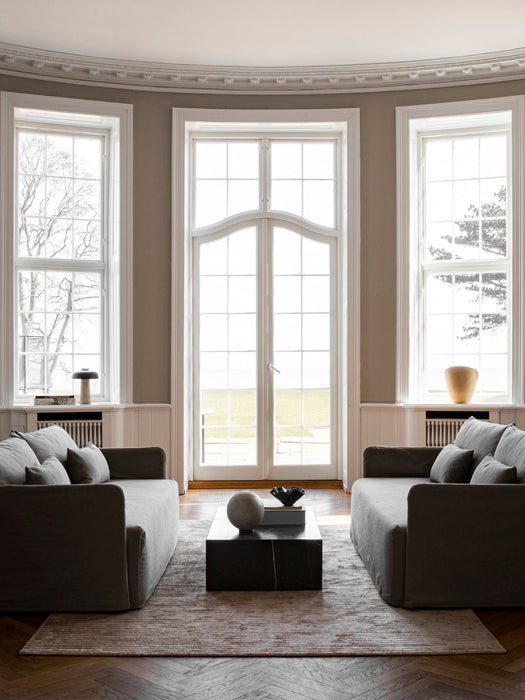 The Plinth Low in black marble, styled as a coffee table between two grey sofas in an elegant room with tall arched windows.