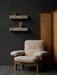 A cream sheepskin Brasilia Lounge Chair in a dark room with two marble Plinth Shelves on the wall and a rattan screen.