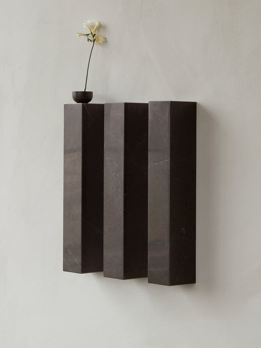 The Plinth Shelf, a wall-mounted sculptural piece in dark marble, styled with a single flower in a small wooden vase on top.