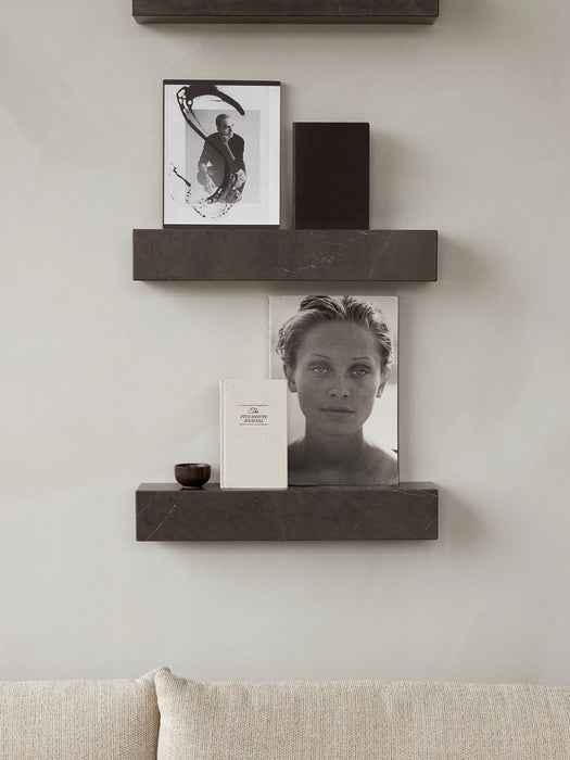 Two dark marble Plinth Shelves mounted on a light grey wall, styled with books, art, and a small decorative bowl.