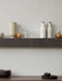 A dark marble Plinth Shelf holds Bottle Grinders, a Cyclades Vase and fruit. Below, New Norm Dinnerware sits on a table.