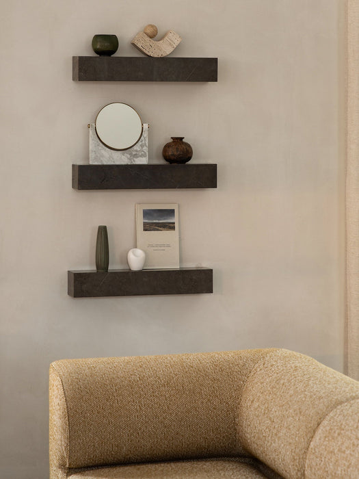 Three dark marble Plinth Shelves, styled with a Pepe Marble Mirror and decor, above the corner of a yellow Eave Sofa.