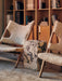Two wooden Knitting Chairs with off-white sheepskin upholstery flank a marble Plinth side table in a cosy, book-lined room.