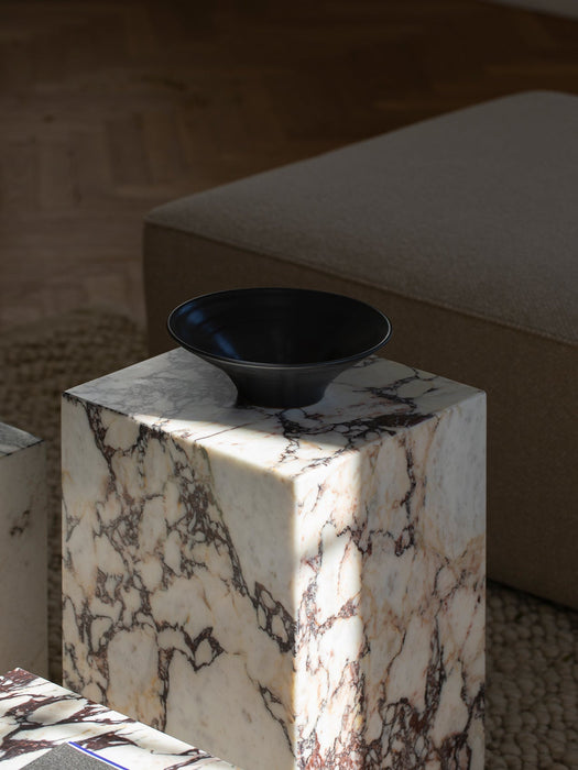 The black Échasse Bowl from Audo CPH sits on a Calacatta Viola marble Plinth, casting a shadow in a sunlit living room.