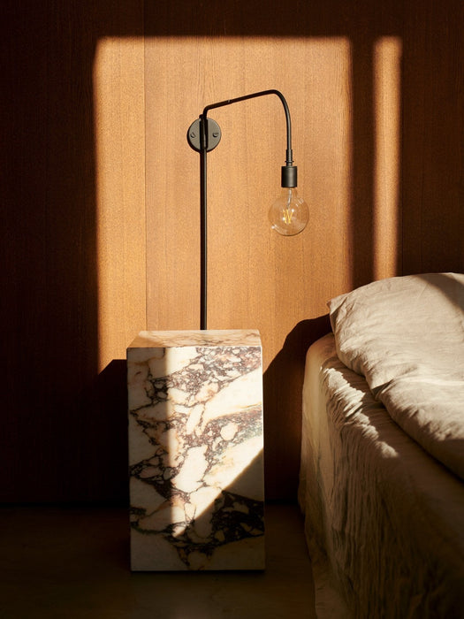 A bedroom scene featuring the black Staple Lamp and a tall marble Plinth as a bedside table, with dramatic natural light.